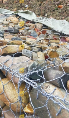 Крупный план сетки двойного кручения и каменного наполнителя – прочная структура габионной подпорной стены для защиты склонов от эрозии в Агое.